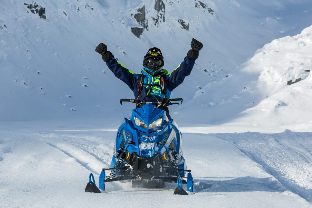 Snowmobiler raising arms in triumph on a snowy mountain trail.